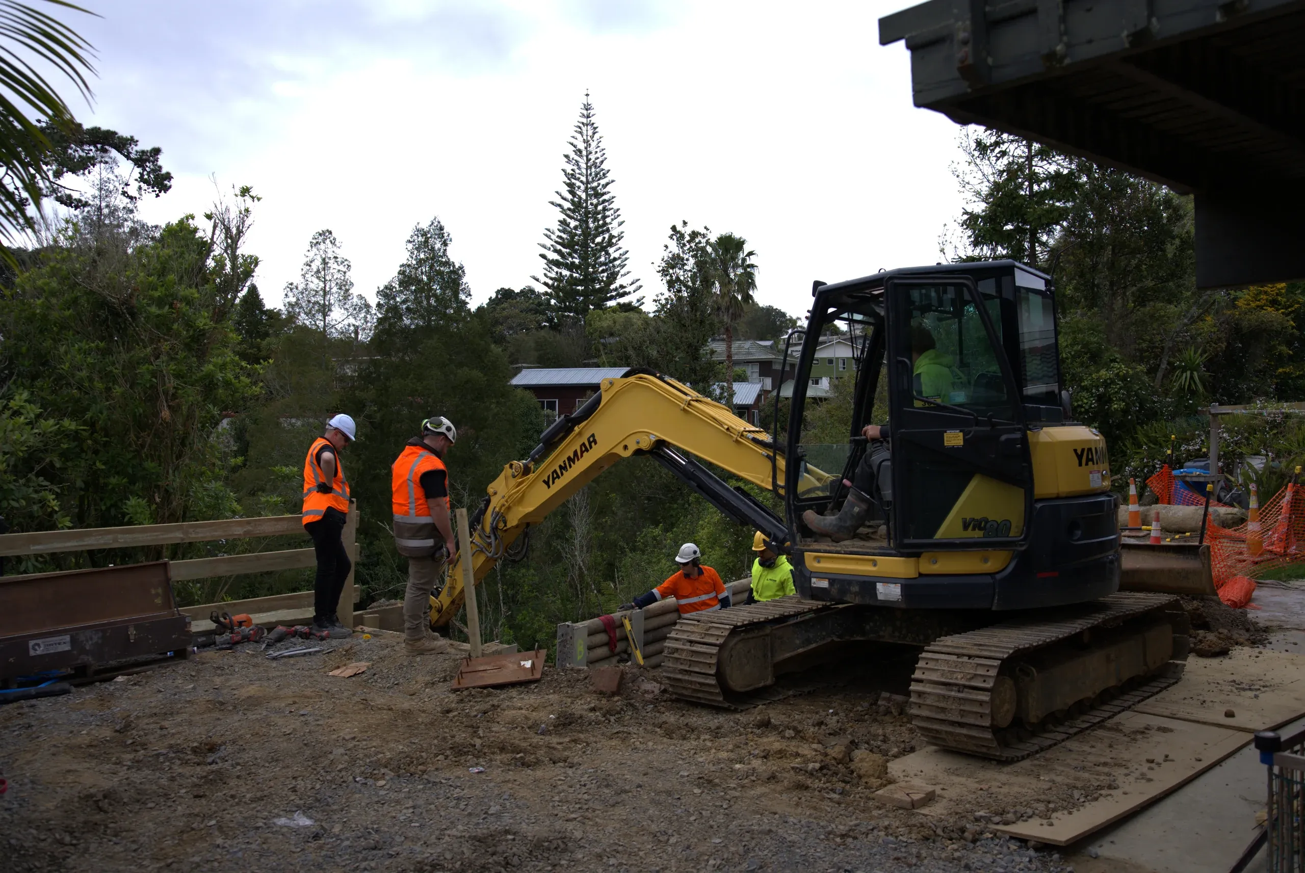 Excavator and crew working the platform below the house deck as the retaining wall progresses.