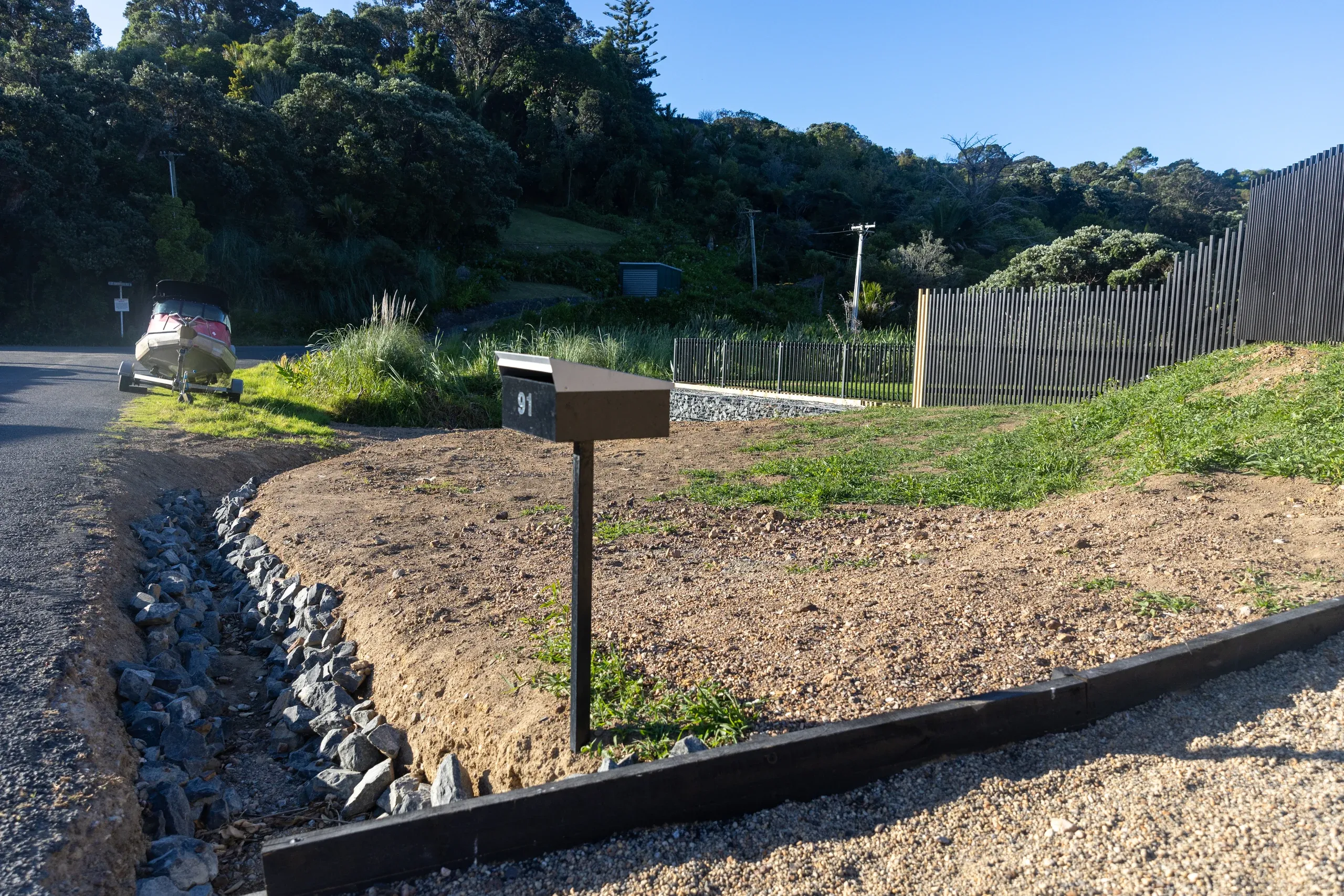 Rock swale and timber edging along the completed driveway, with the retained bank planted behind.