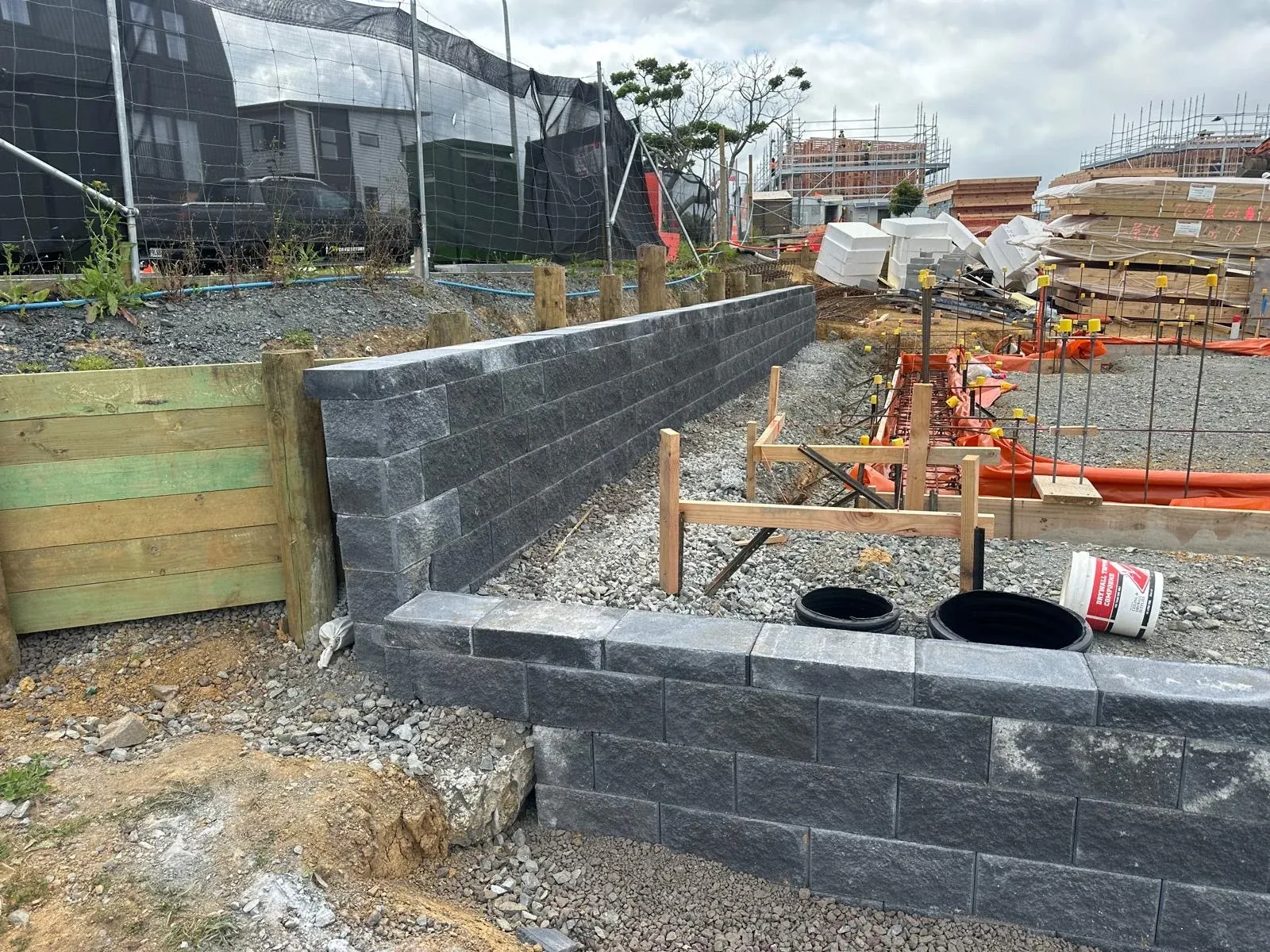 Keystone block wall meeting an existing timber retaining wall, showing the two systems tied together across a level change.