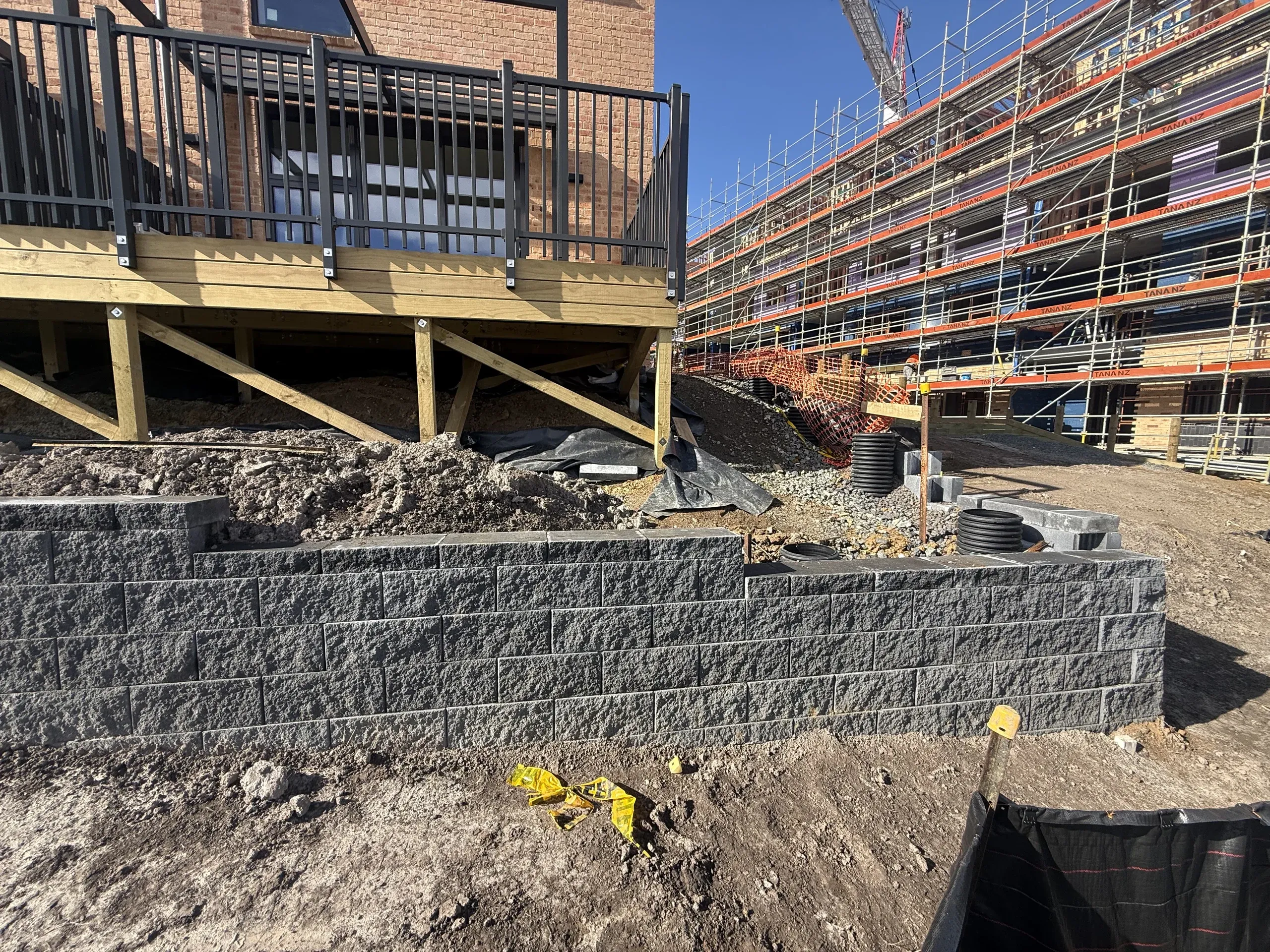 Finished Keystone block wall retaining the ground below a new timber deck, with a scaffolded apartment block under construction beyond.