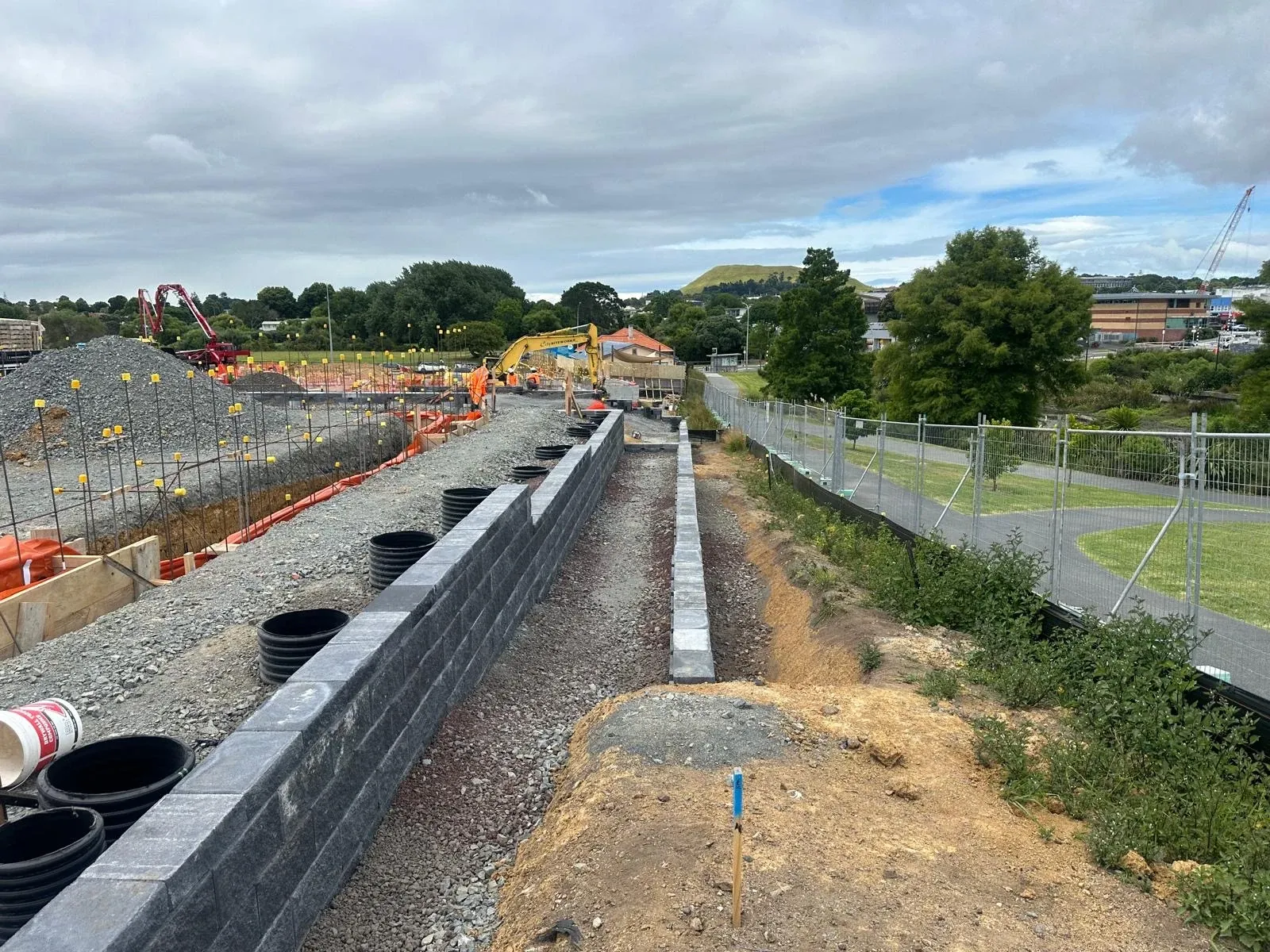 Long Keystone block wall running across the subdivision with an excavator working the platform beyond and Maungarei on the skyline.