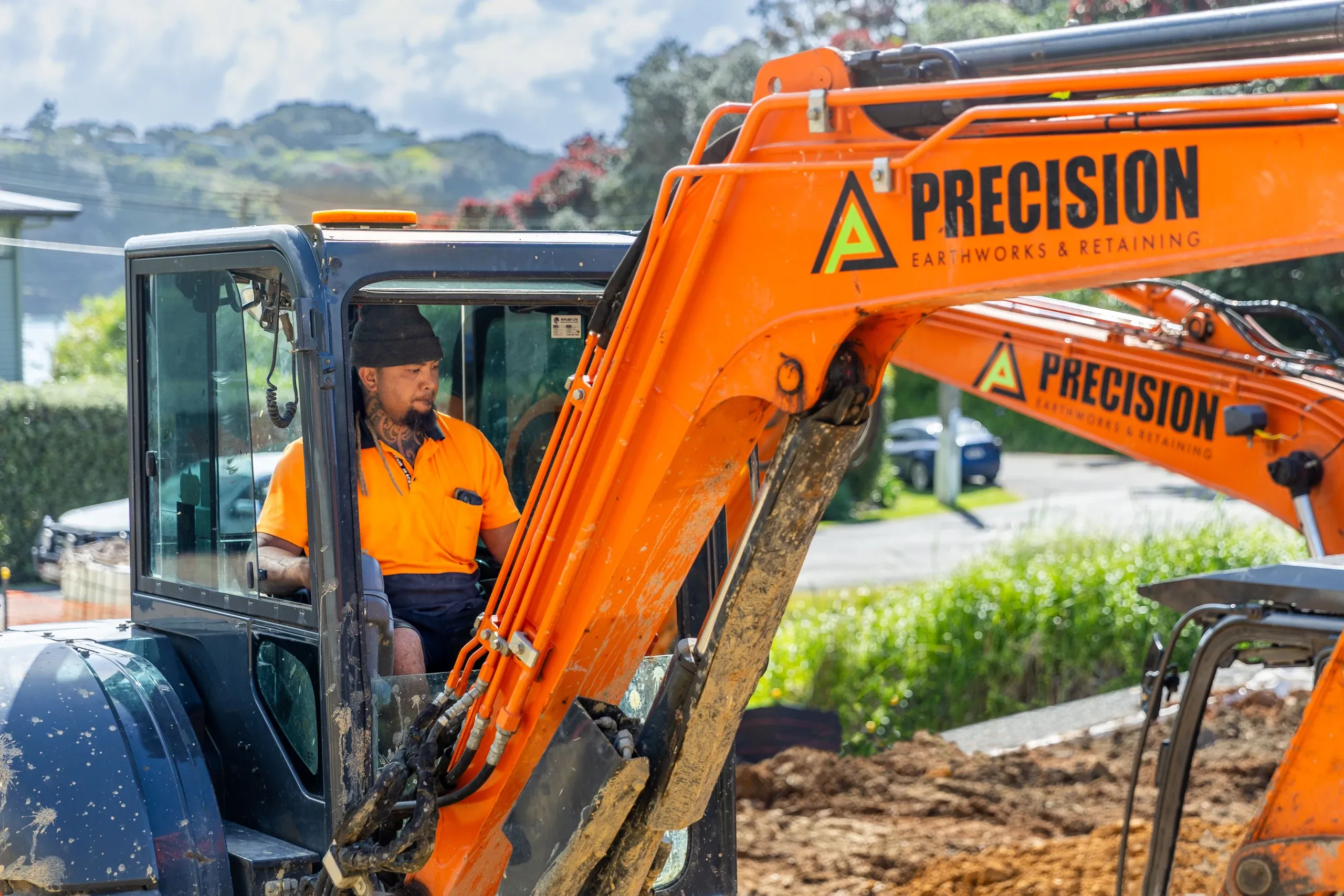 A Precision operator at the controls, the Waiheke coastline and bush framing the cab.